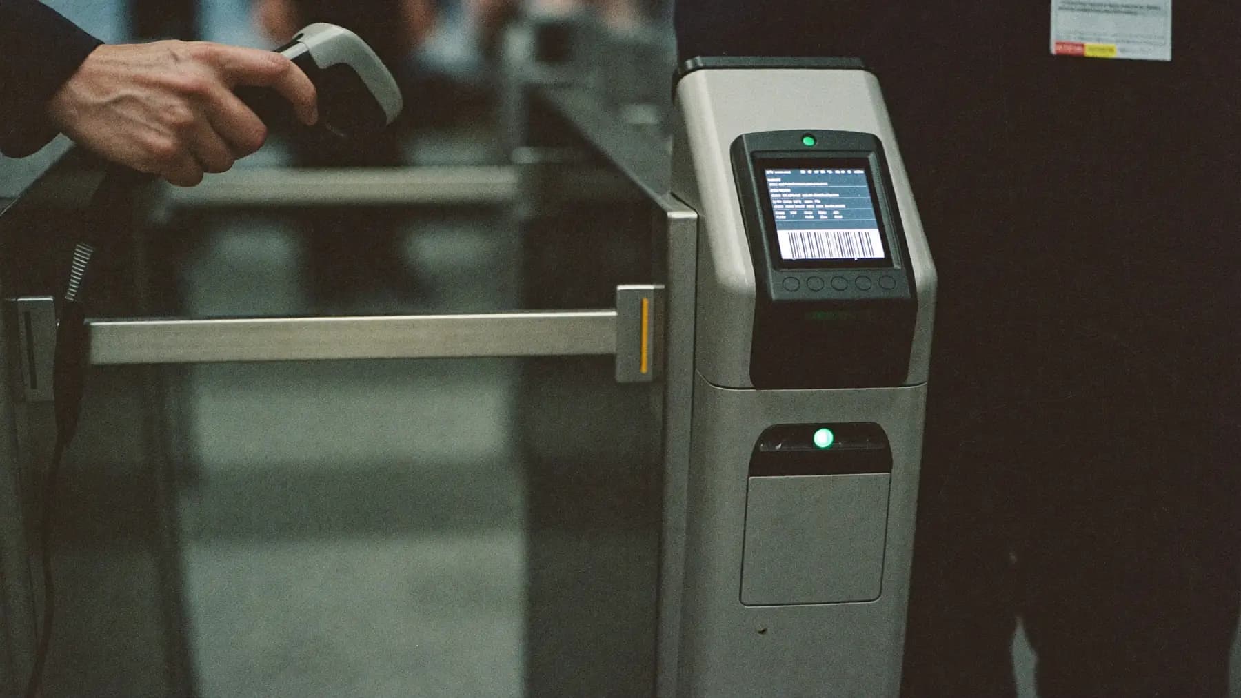 A speed-gate turnstile at a conference entrance with a lit RFID reader and a handheld scanner resting on the post.