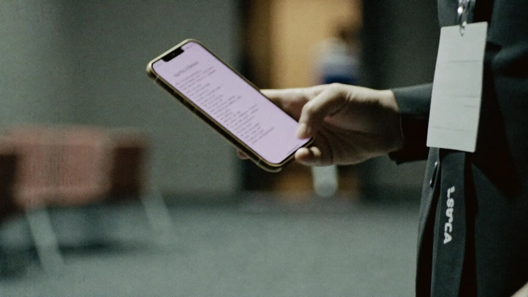 A delegate's hand holding a phone at a conference, lanyard and badge at the edge of frame, session room blurred behind.
