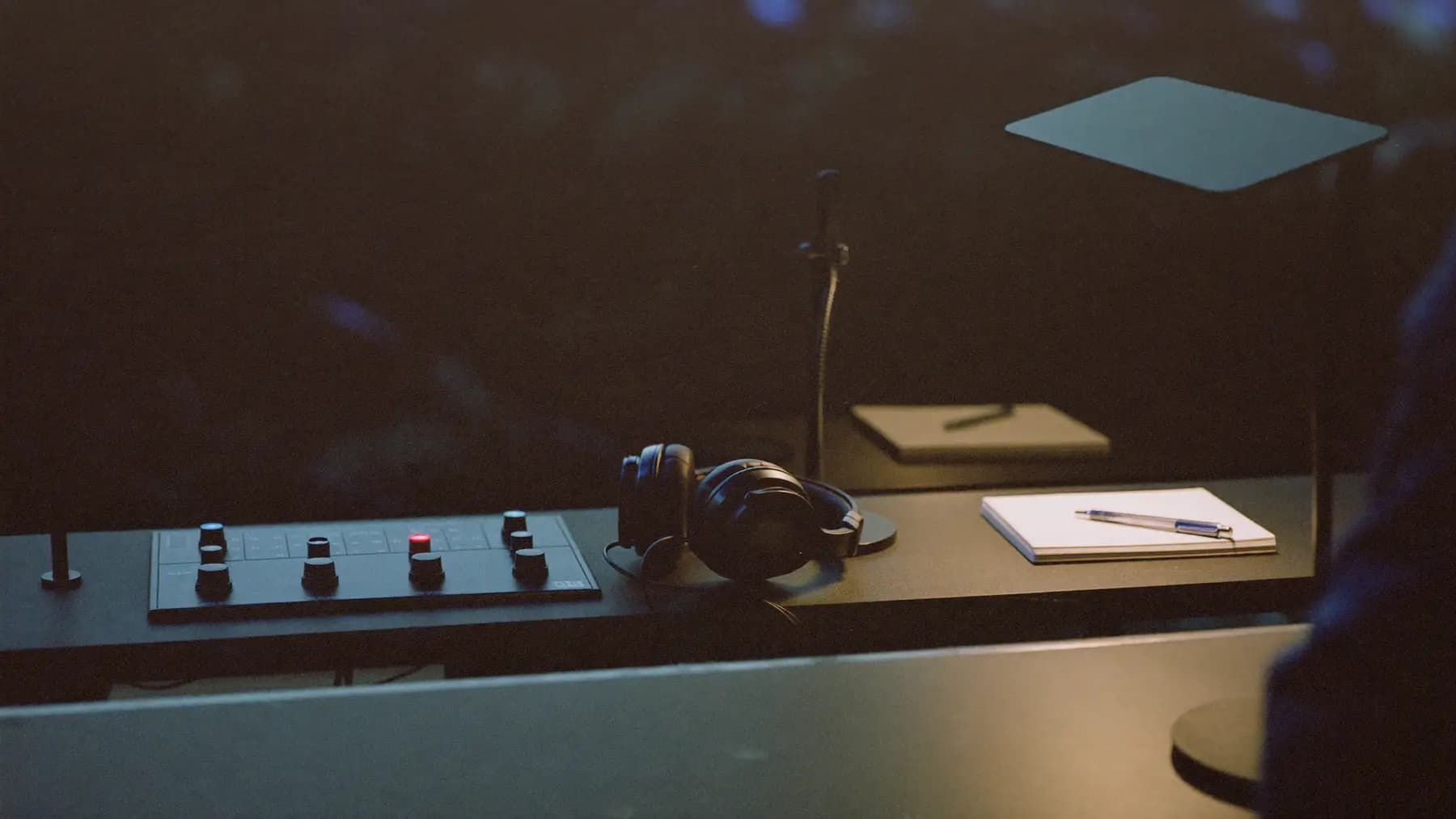 An interpretation booth seen through glass: headphones resting on a console beside a microphone and a marked-up notepad.