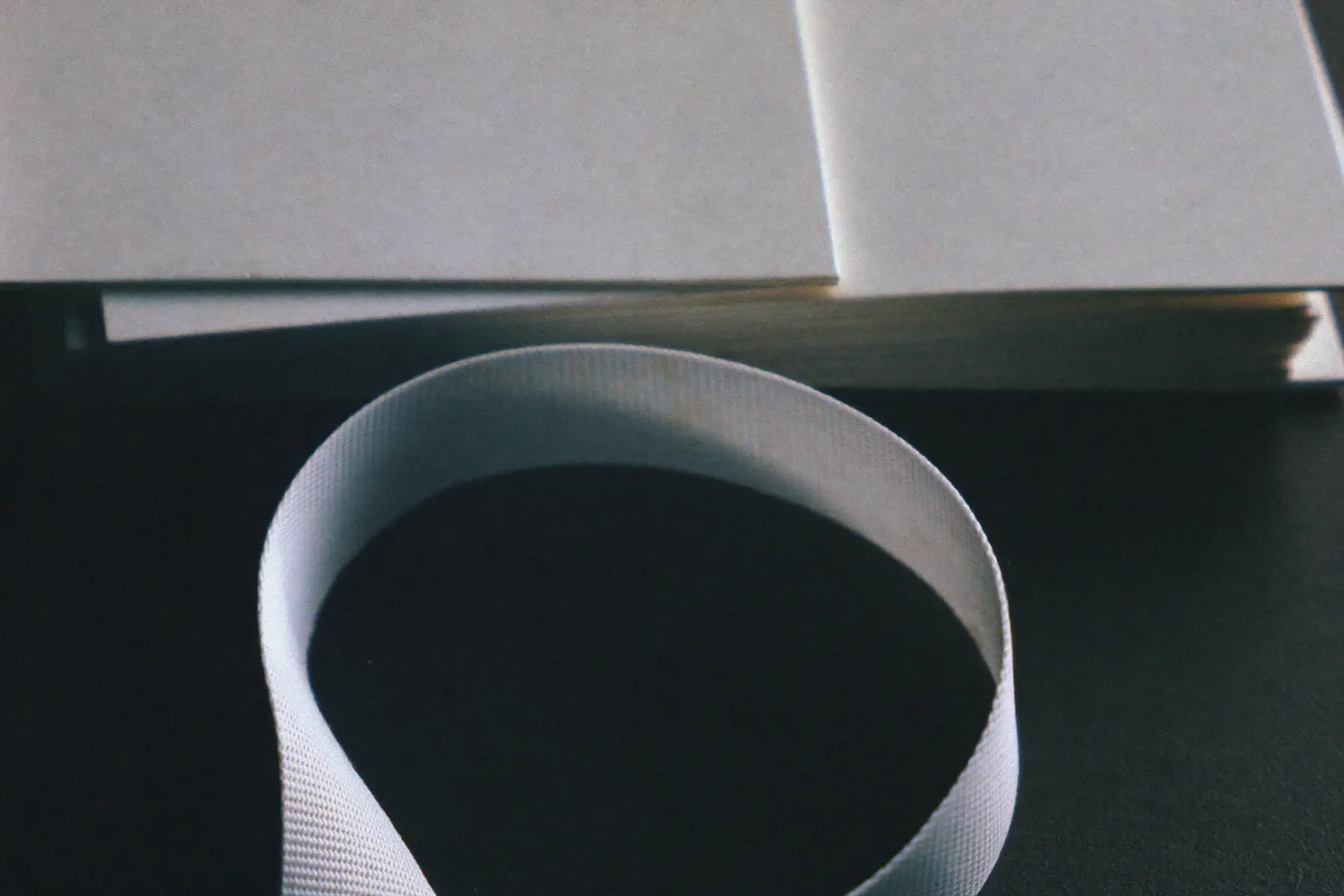 Macro detail of a coiled woven lanyard ribbon in front of the cut edges of a stack of blank card stock.