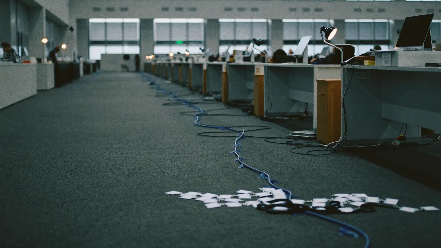 A long row of empty event check-in desks before doors open, laptops and badge printers set out, cable runs taped across the carpet.