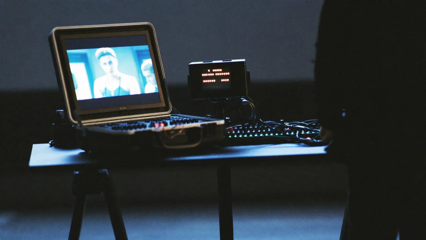 An open road case holding a video switcher and encoder, coiled cables and a small confidence monitor showing the stage.
