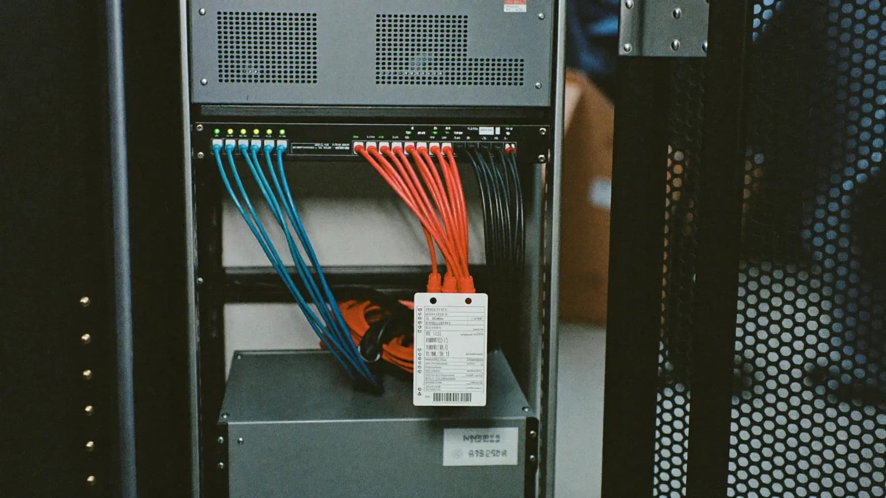 An open network rack deployed at a venue, patch panel neatly dressed with coloured ethernet, switch LEDs lit, a UPS below.