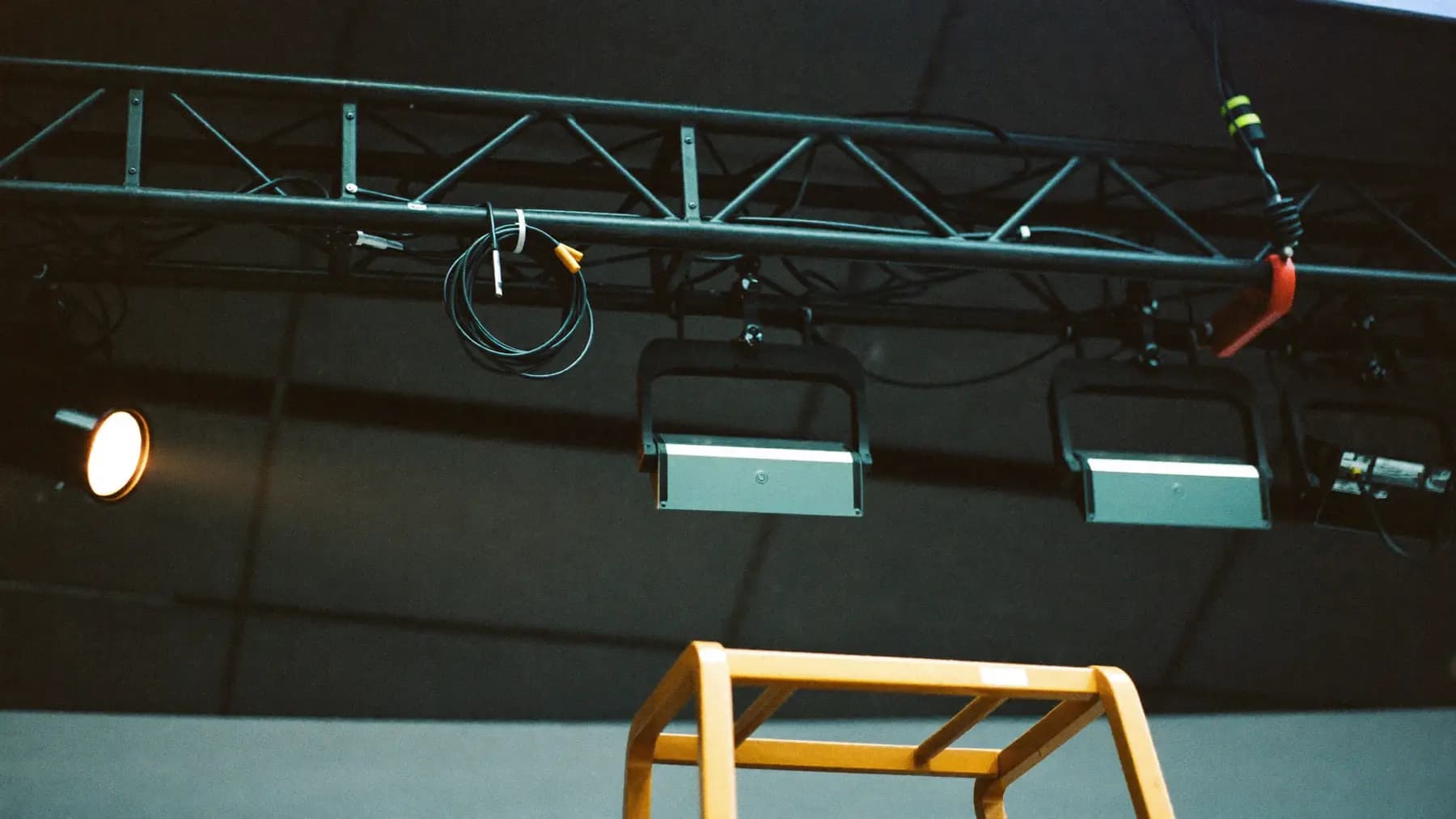 Lighting truss above a conference stage during load-in, fixtures clamped and safety-bonded, cable slung over a bar.