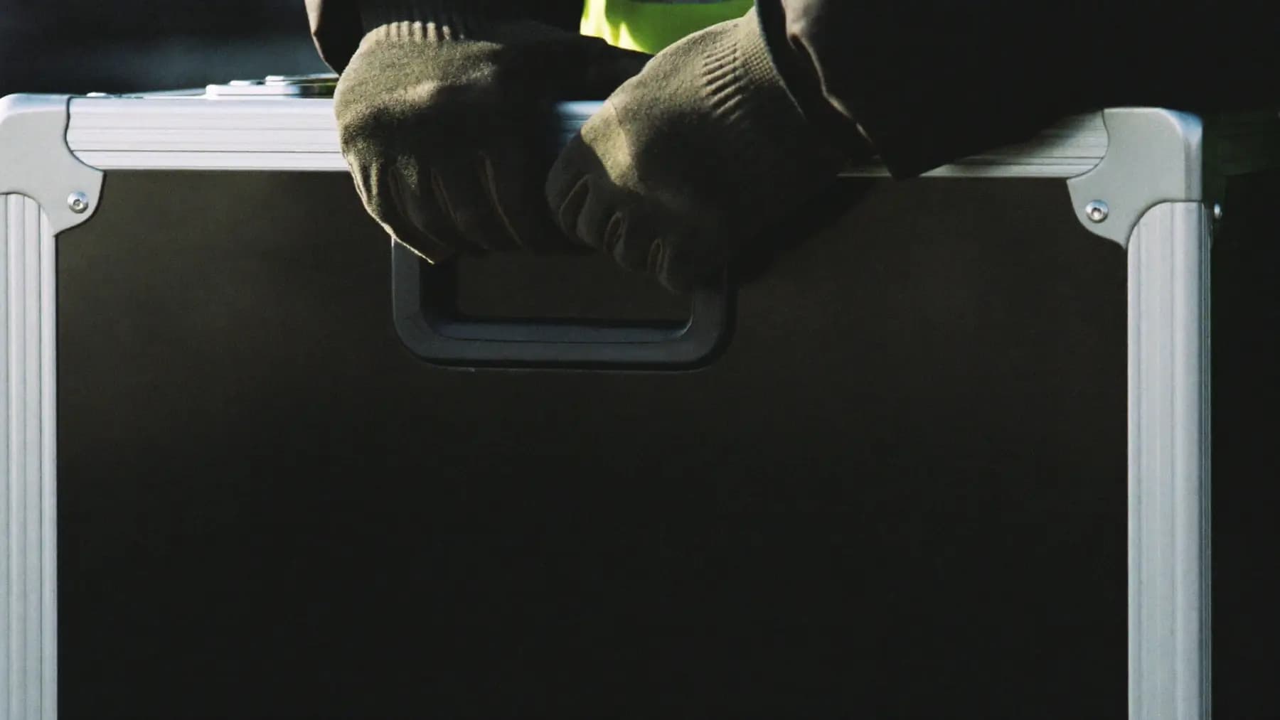 Close crop of two gloved hands gripping the handle of a black road case during load-in.